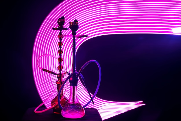 Two hookahs with shisha coals pink neon lighting on a dark background