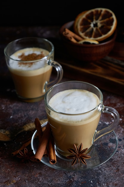 Two hot cappuccino coffee with foam , cinnamon , sugar and anise on a brown surface