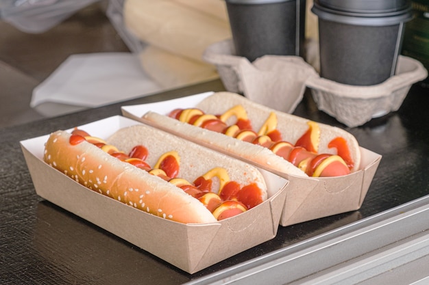 Two hot dogs in a cardboard box on the counter of a street food takeout cart.