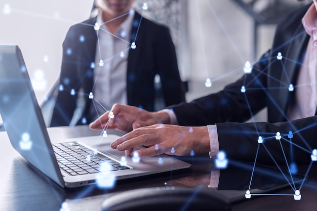 Two HR specialists in formal wear analyzing the recruitment market using laptop to boost the intern program at international consulting company Social networking hologram icons