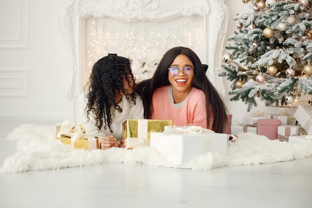 Two indian girls in eyeglasses lay on a floor near Christmas tree