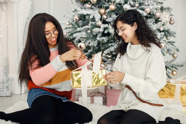 Two indian girls in eyeglasses sitting near Christmas tree