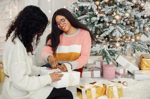 Two indian girls in eyeglasses sitting near Christmas tree