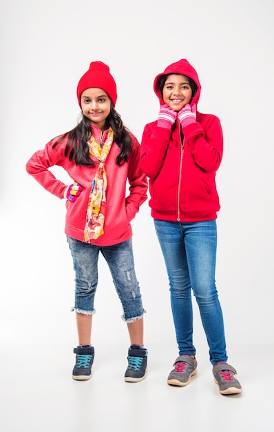 Two Indian little girls in warm cloths standing against white background