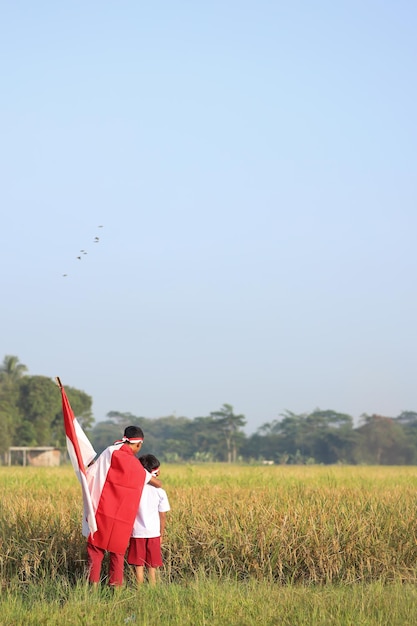 Two Indonesian school student holding flags during independence day in the rice field. Proud primary