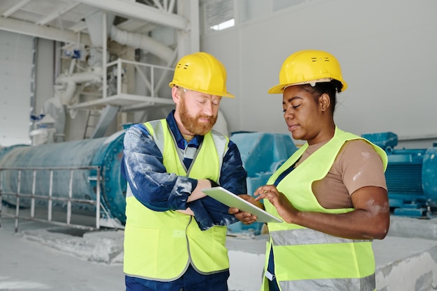 Two intercultural engineers in workwear and safety helmets networking