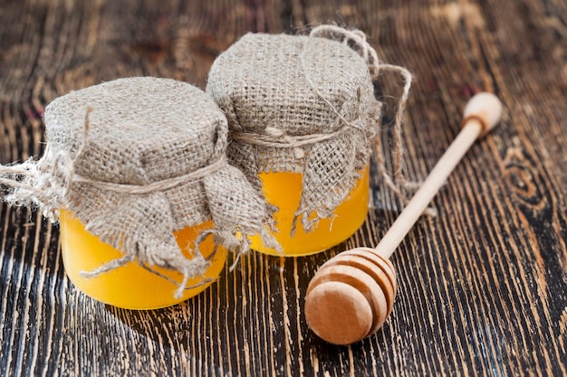 Photo two jars of honey made of glass are covered with lids and a linen cloth, fresh bee honey packed in glass jars