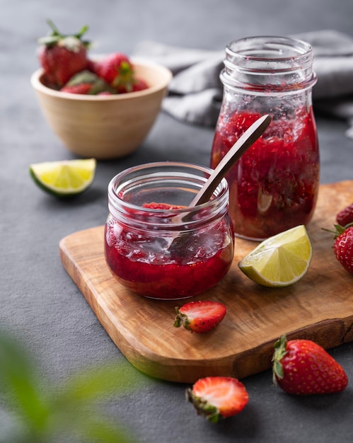 Two jars of strawberry jam on a wooden board on a dark background with fresh berries Homemade sweets