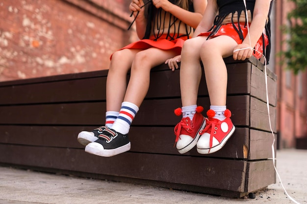 Two kids are sitting resting on a city bench Children's sports shoes are red and black with laces