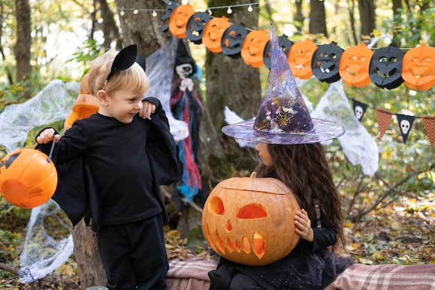 two kids girl and boy in halloween costume with pumpkins in halloween decorations outdoor