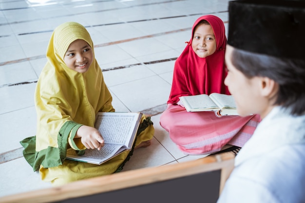 Two kids learning to read quran and point to black board with muslim teacher or ustad in mosque