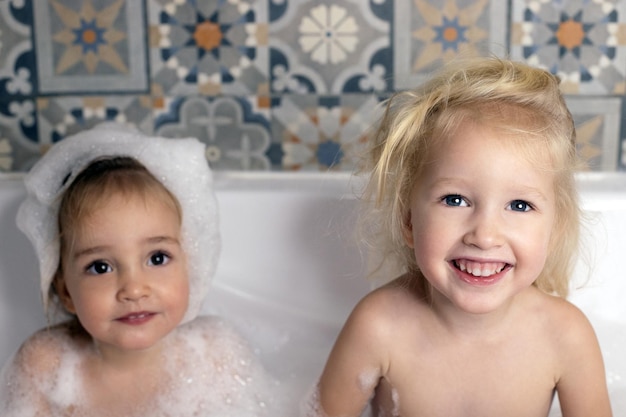 Two kids little girls sisters having fun in bathroom playing with bath foam kids personal care