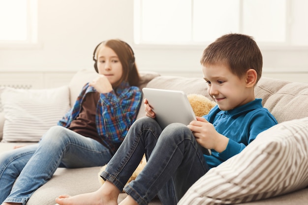 Two kids with gadgets on couch at home