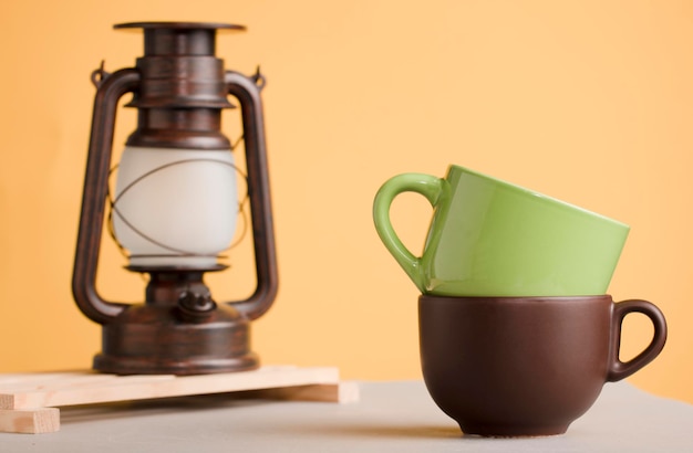 two large brown and green mugs on wood with lamp cande yellow 
background