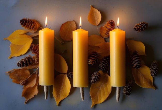 Two lit beeswax candles on a concrete surface with dried leaves scattered around them