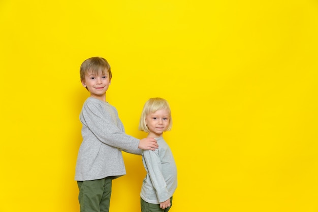 Two little boys in a great mood. The older brother holds his brother by the shoulders.