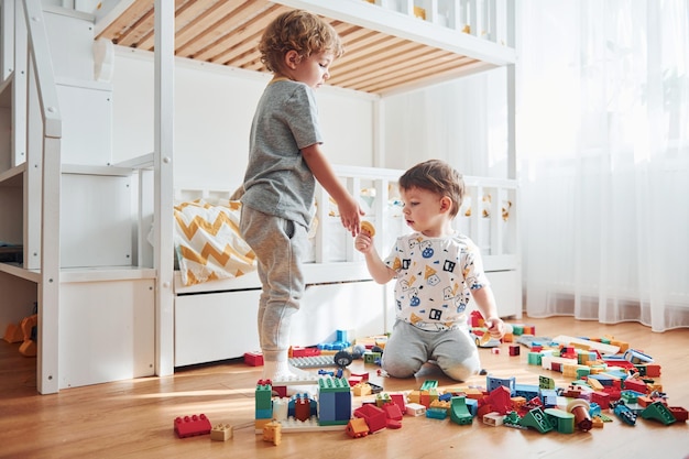 Two little boys have fun indoors in the bedroom with plastic construction set