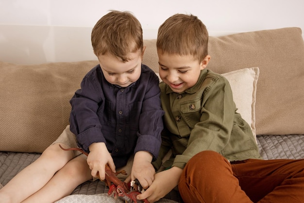 Photo two little and cute caucasian boys playing with dinosaurs at home. interior and clothes in natural earth colors. cozy environment. children having fun with toys, two friends.