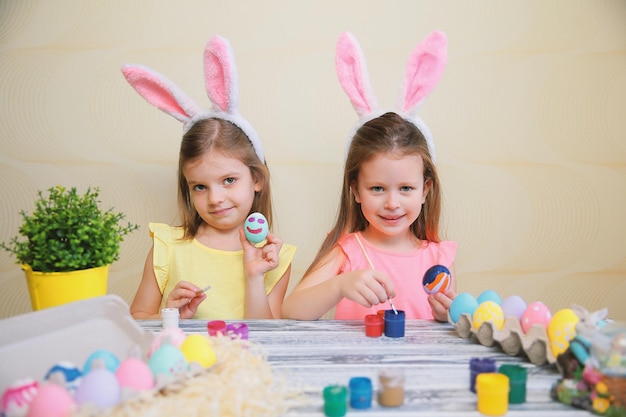 Two little cute girls in bunnies ears paint and decorate easter eggs preparing for easter