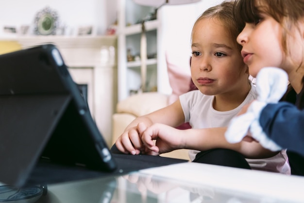 Two little girls attentively watching a video on a tablet in their living room Concept of childhood technology learning having fun the Internet and connectivity