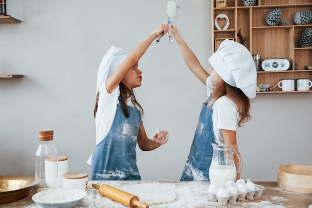 Two little girls in blue chef uniform kneading dough on the kitchen