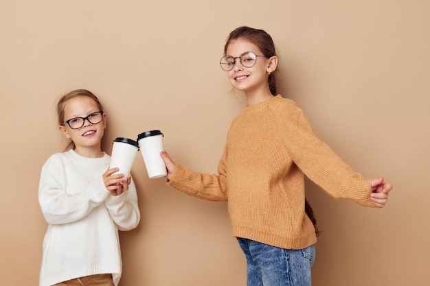 Two little girls disposable glasses posing beige background