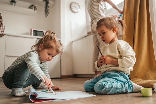 Two little girls drawing on the kitchen floor