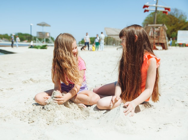 Two little girls have fun on the sandy beach children play with sand