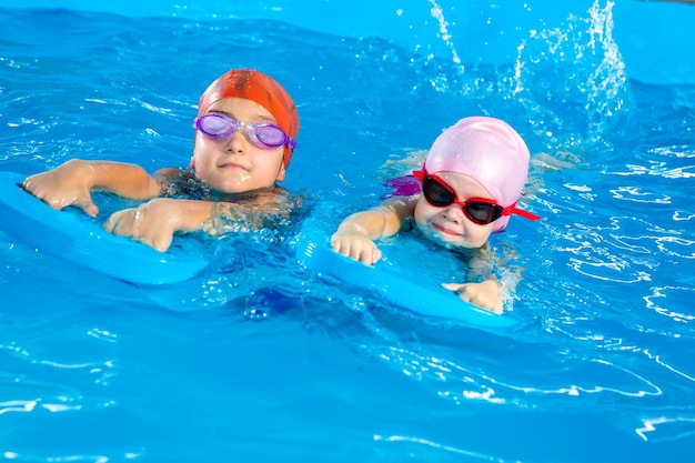 Two little girls having fun in pool learning how to swim using flutter boards