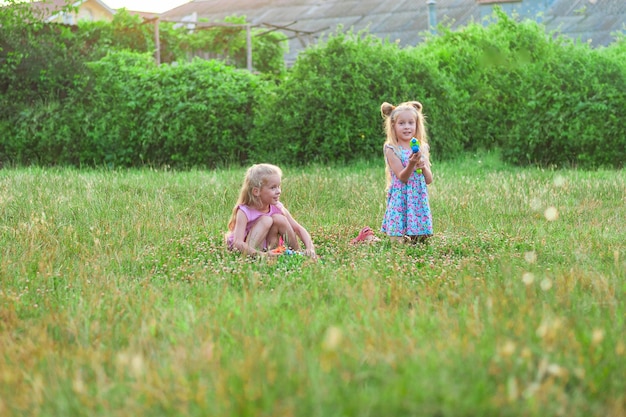 Photo two little girls play in the summer on a green meadow with water pistols