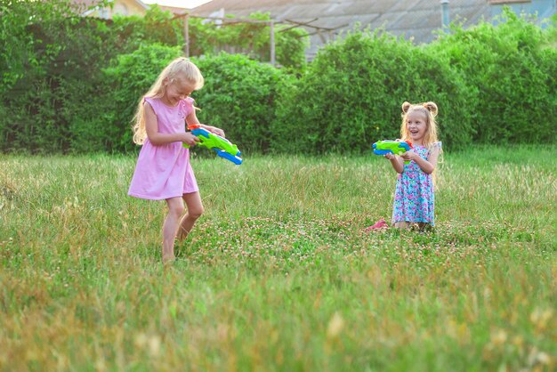 Photo two little girls play in the summer on a green meadow with water pistols