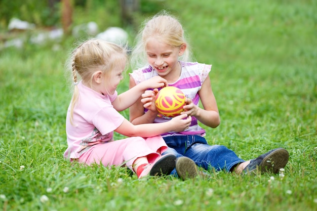 Two little girls playing in the grass  with the ball