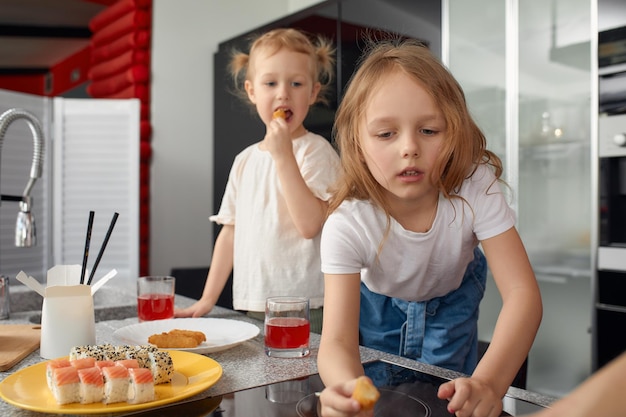 Two little girls siblings having fun and eating on the kitchen at home with japanese food