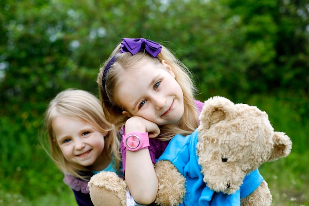 Two little girls siblings hug teddy bear at nature