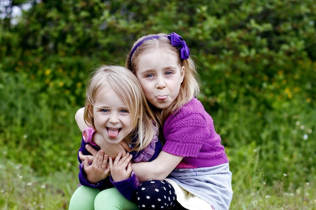 Two little girls siblings show tongues outdoors