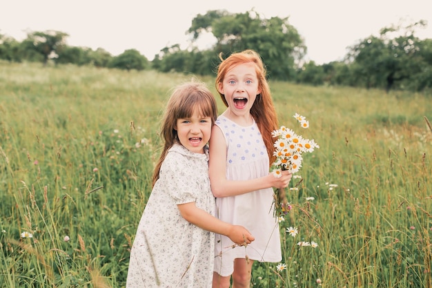 Two little girls sisters play and have fun on the grass holding hands in light dresses.