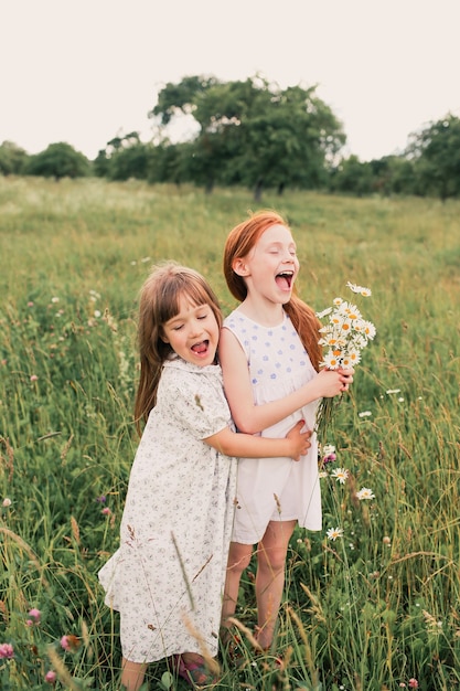 Two little girls sisters play and have fun on the grass holding hands in light dresses.