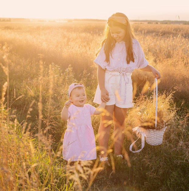 Two little sisters in summer field at sunset