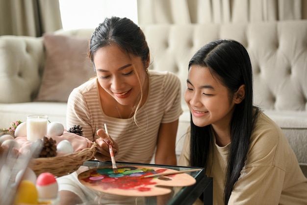 Two lovely Asian sisters enjoy painting an Easter egg together in their house Easter holiday