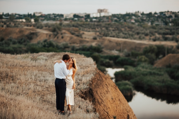 Two lovers embracing on top of a hill overlooking the city and river.