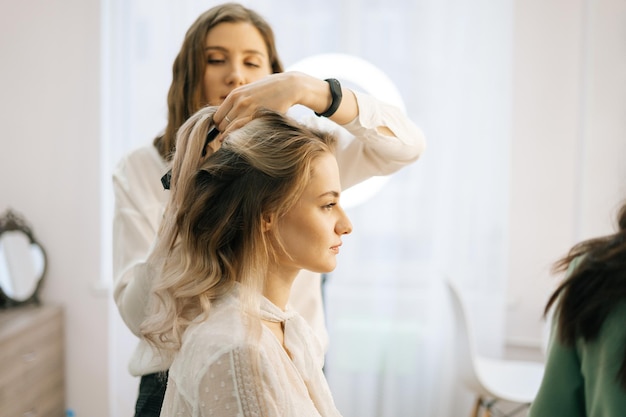 Two make-up artistes applies hair and makeup to the bride in dressing room. Concept of backstage work.