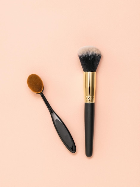 Two makeup brushes on a light pastel background