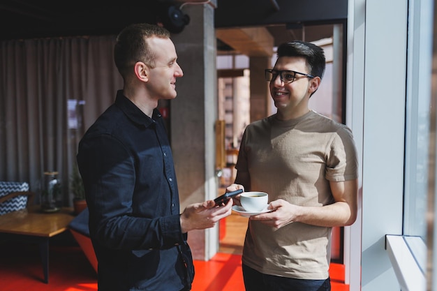 Two male businessman managers stand near the window in a modern office and discuss a new project Two men with glasses are talking about a new business