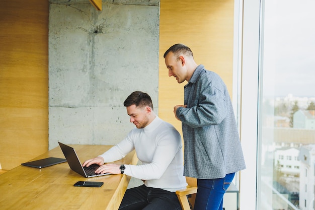 Two male colleagues while working with a laptop in the office Two goaloriented entrepreneurs collaborate in a modern workspace Two young businessmen work in a bright office