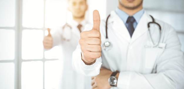 Photo two male doctors standing as a team with thumbs up in hospital office and ready to help patients medical help best disease treatment and medicine concept