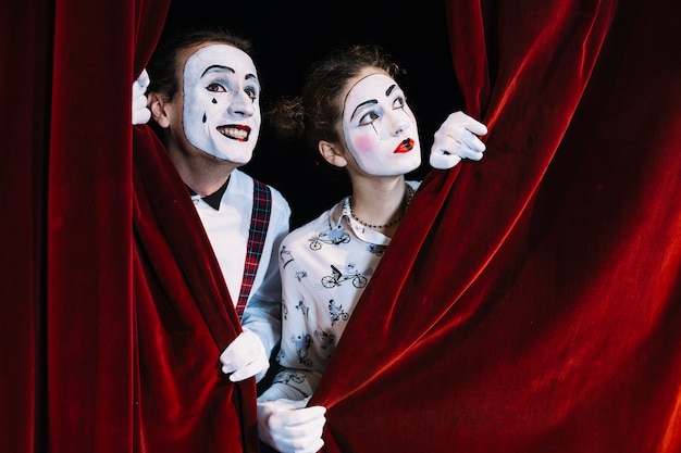 Two male and female mime artist looking through red curtain