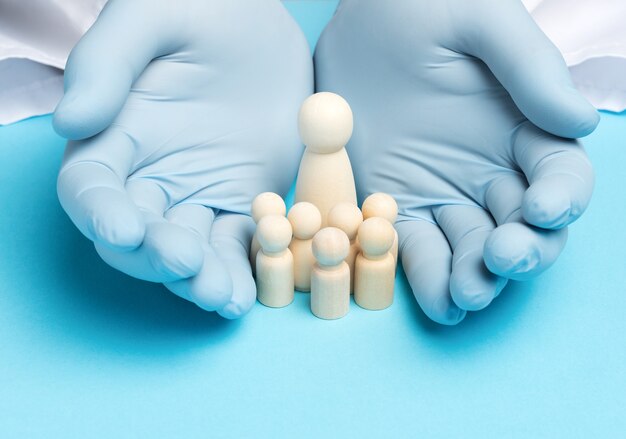 Two male hands in blue latex gloves and wooden figurines of a woman with children, the concept of a large family and insurance