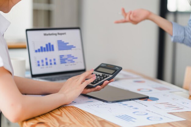 Photo two marketing professionals discussing marketing report with bar graphs with a laptop showing business performance dashboard in the background