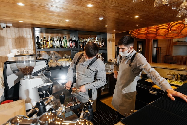 Two masked baristas prepare exquisite delicious coffee at the bar in the coffee shop The work of restaurants and cafes during the pandemic