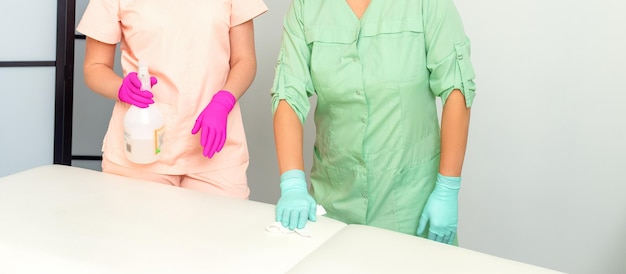 Two medical workers disinfect the patient's couch with sanitizer spray and a clean napkin Health and hygiene concept